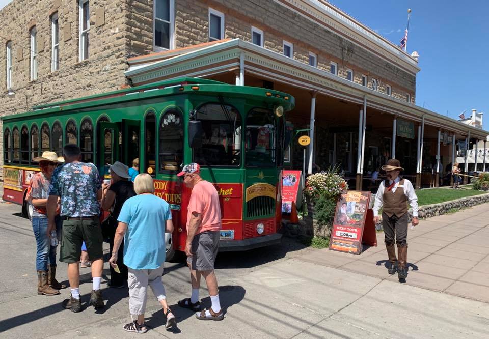 Elderly visitors are walking next to the Cody Trolley Tour bus at Sheridan Avenue.