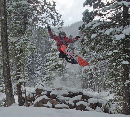 A snowboarder launching from a jump on a snowy hill