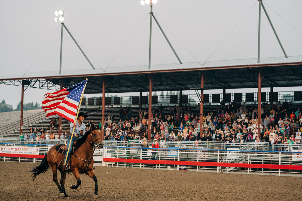 A woman rides a horse while carrying the American flag at the Cody Nite Rodeo