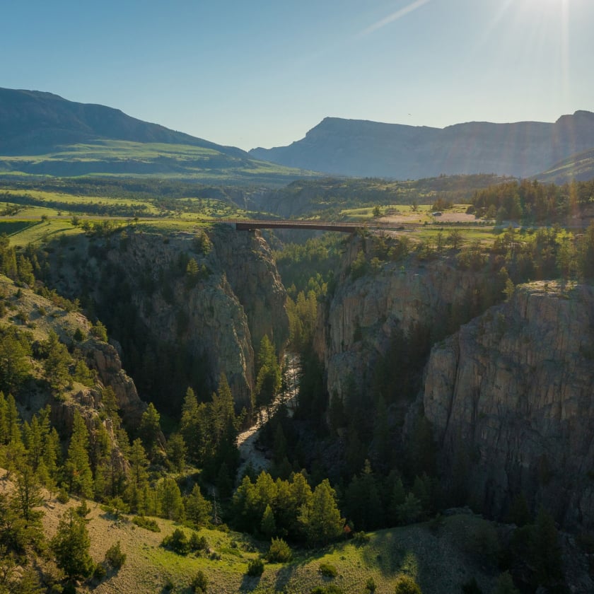 Sunlight bathes a beautiful canyon, showcasing a bridge that arches over the rocky landscape.