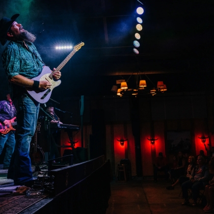 A bearded man strumming a guitar passionately on stage, captivating the audience with his music