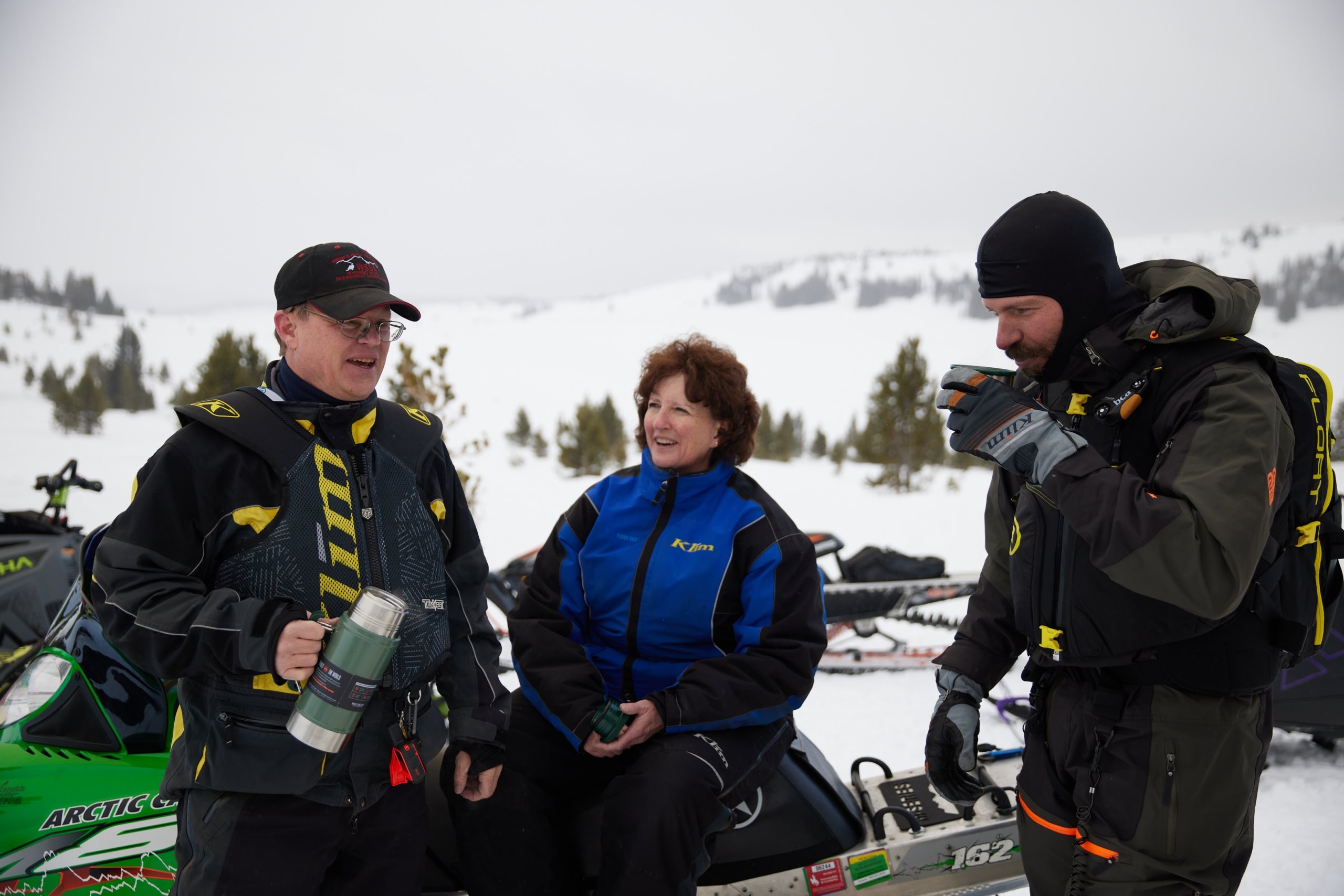 3 people taking a coffee break while snowmobiling