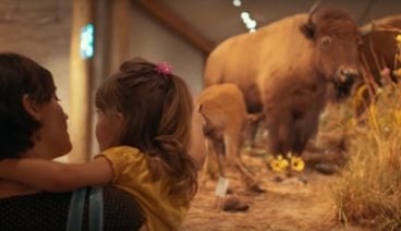 A mother holder her child while looking at a preserved buffalo in a museum