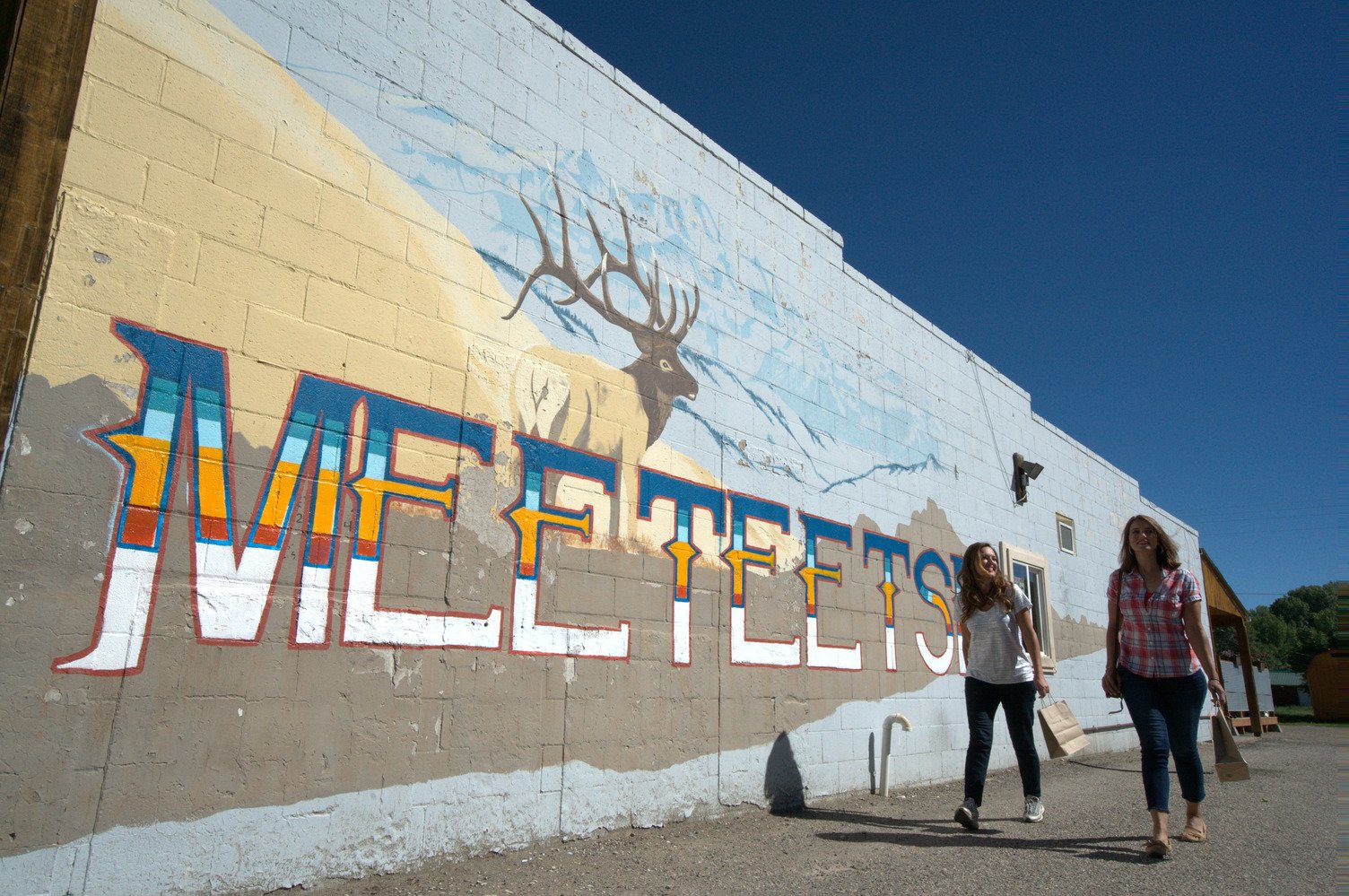 Two women walk beside a wall mural in Meeteetse in Cody Yellowstone.