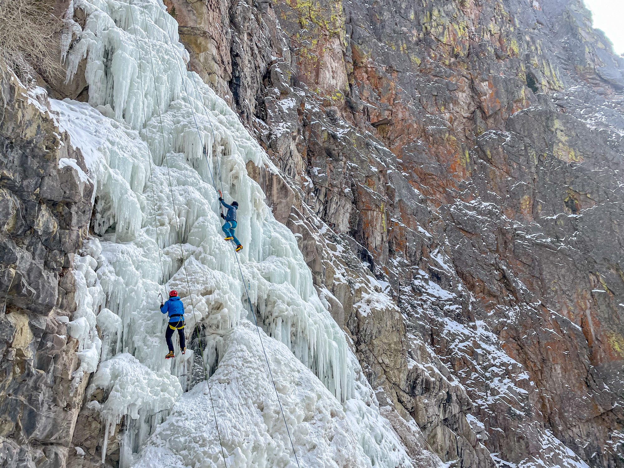 Two people climb a frozen waterfall in Cody Yellowstone