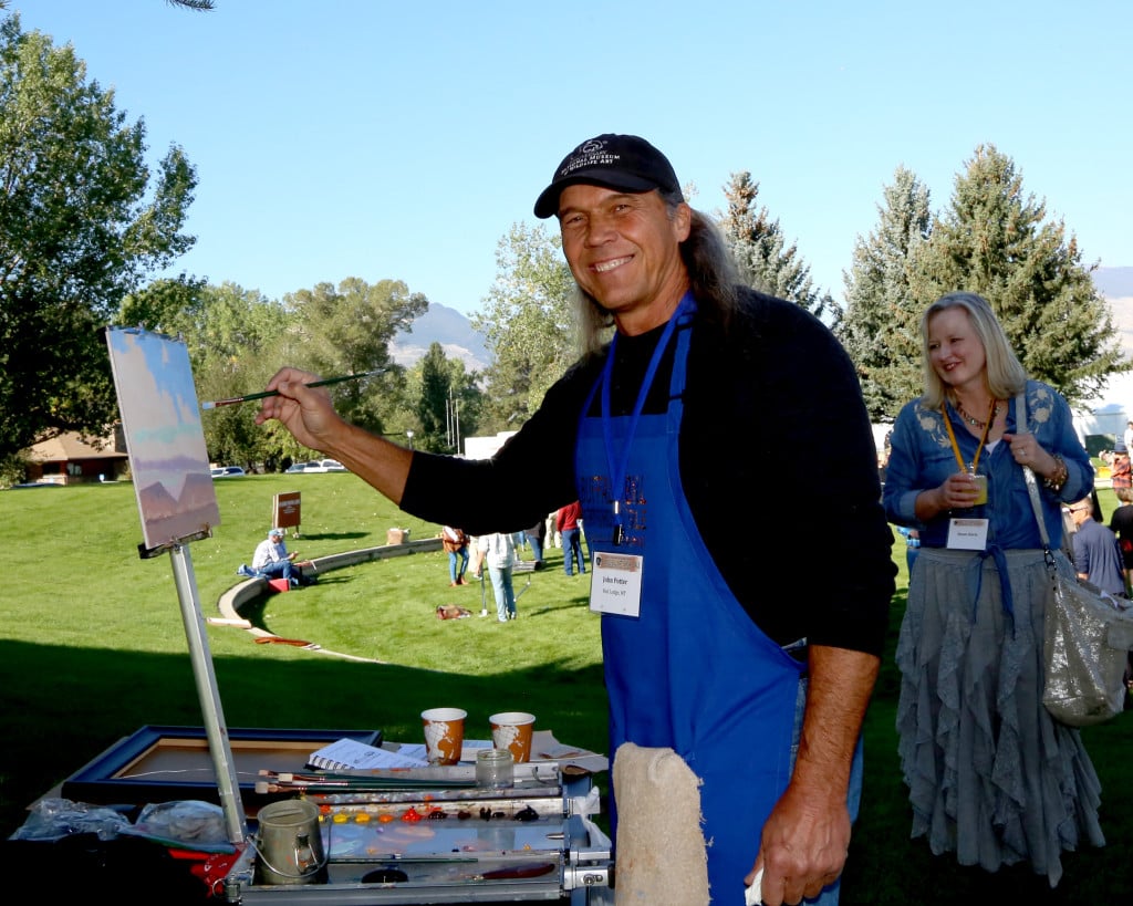 A man wearing a blue apron painting a landscape painting in the park