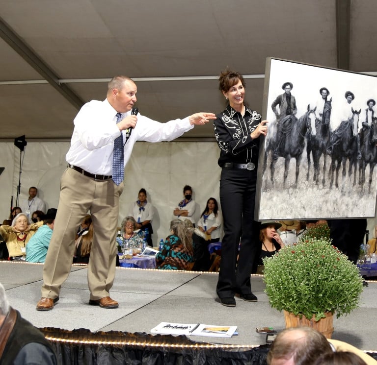 An auctioneer on stage and a woman holding a black and white large frames photo.