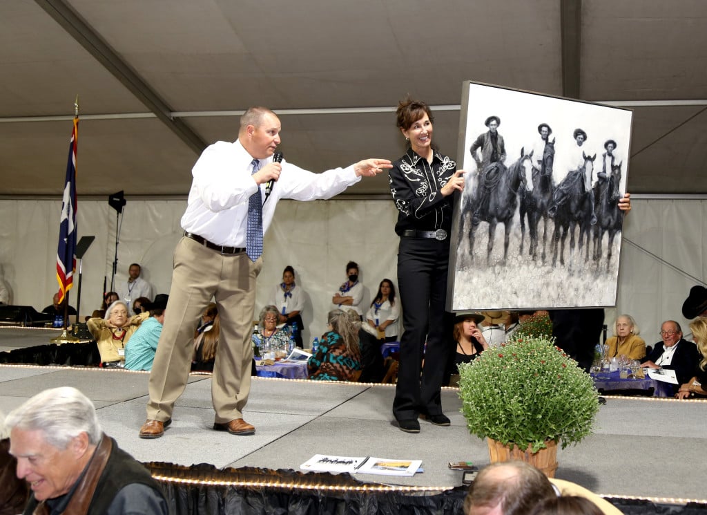 An auctioneer on stage and a woman holding a black and white large frames photo.