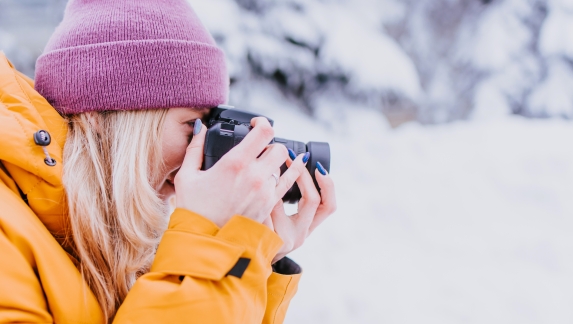 Cheerful girl photographer in a yellow jacket takes pictures of winter
