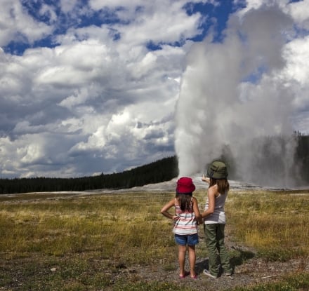 Backshot of two girls watching the Old Faithful as it erupts