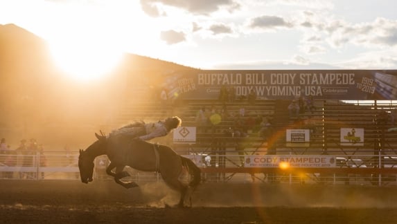 A man rides a horse at the Cody Stampede Rodeo at twilight