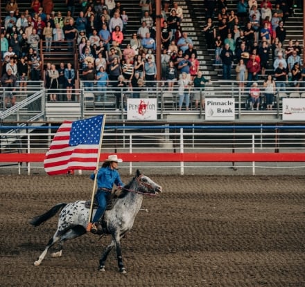 A woman rides a horse while carrying an American flag at the Cody Stampede Rodeo